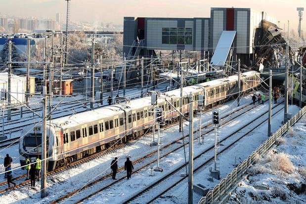 A long shot of a derailed train on snowy tracks as rescue workers inspect the damage.