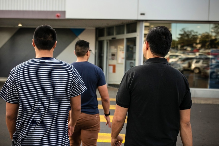 Three men seen from behind walking towards a building.