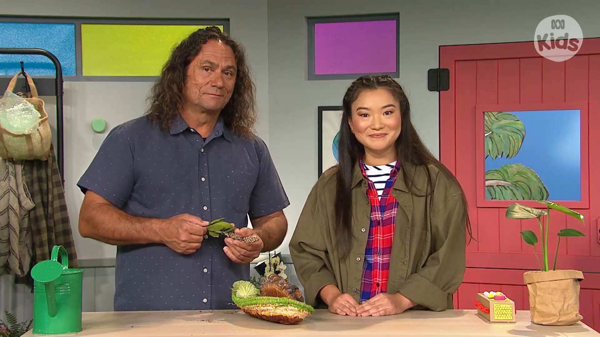 Clarence and Michelle, with some plants in front of them, on the Play School set