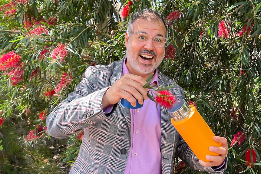 Professor Ghadouani, wearing a pink shirt and a grey blazer, holds a bottle brush flower over his metal drink bottle.