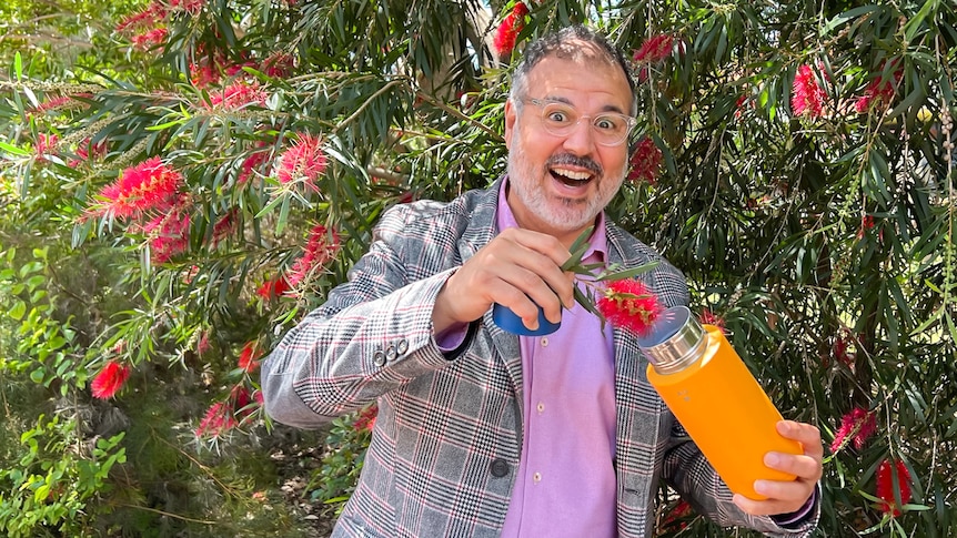 Professor Ghadouani, wearing a pink shirt and a grey blazer, holds a bottle brush flower over his metal drink bottle.