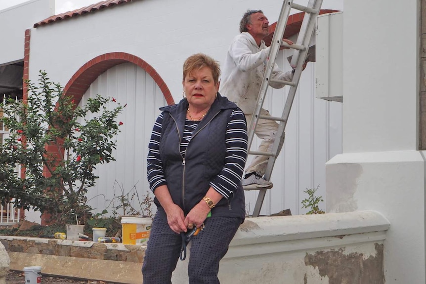 Jeanette Scannell sits on a fence while a painter climbs a ladder behind her.