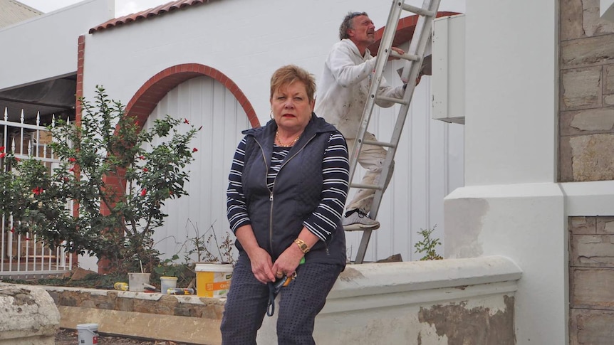 Jeanette Scannell sits on a fence while a painter climbs a ladder behind her.