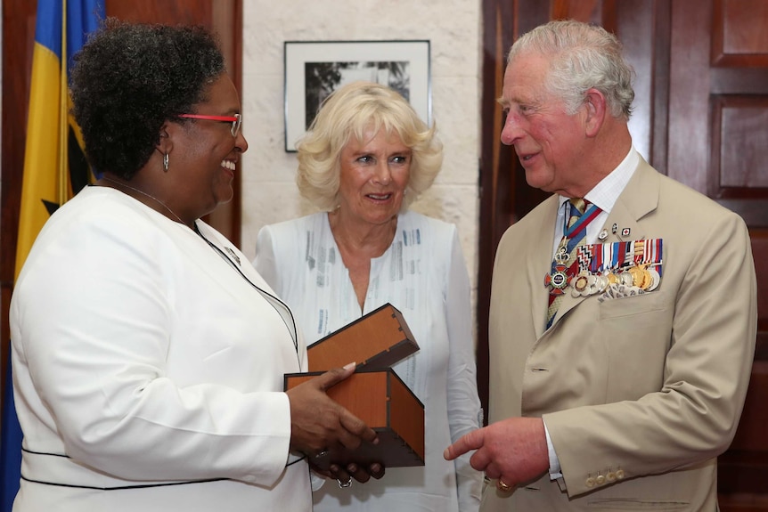 Woman with black hair in white suit hands present to old man with grey hair in beige suit