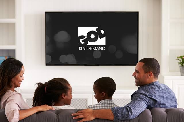 A family sit on a couch in front of a large TV with the God TV logo on it.