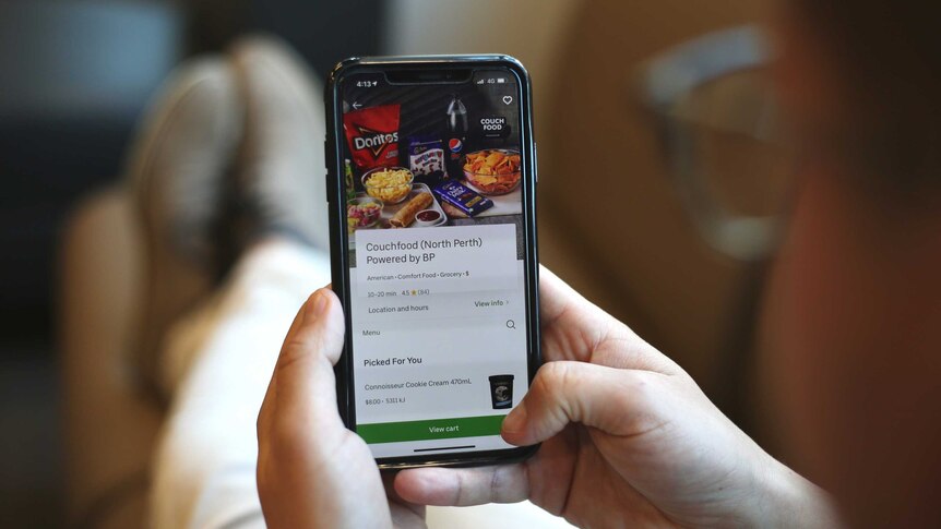A man with glasses sits on a couch ordering food from his iPhone