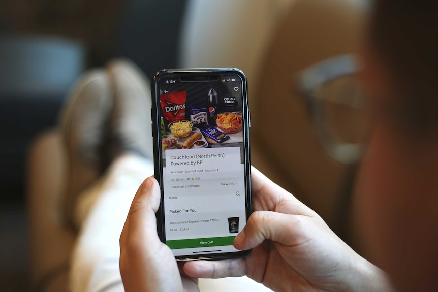 A man with glasses sits on a couch ordering food from his iPhone