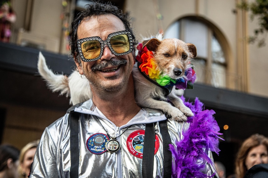A grinning man in a reflective jacket smiles with a dog resting on his shoulders