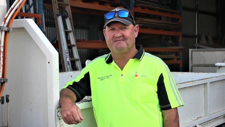 He wears a hi-vis top and leans again a ute tray