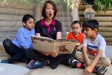 A woman reading a book to three boys.