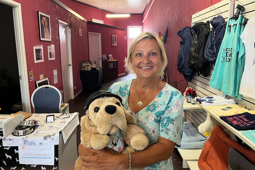 A woman with blonde hair holds a soft toy shaped like a dog in a shpo.