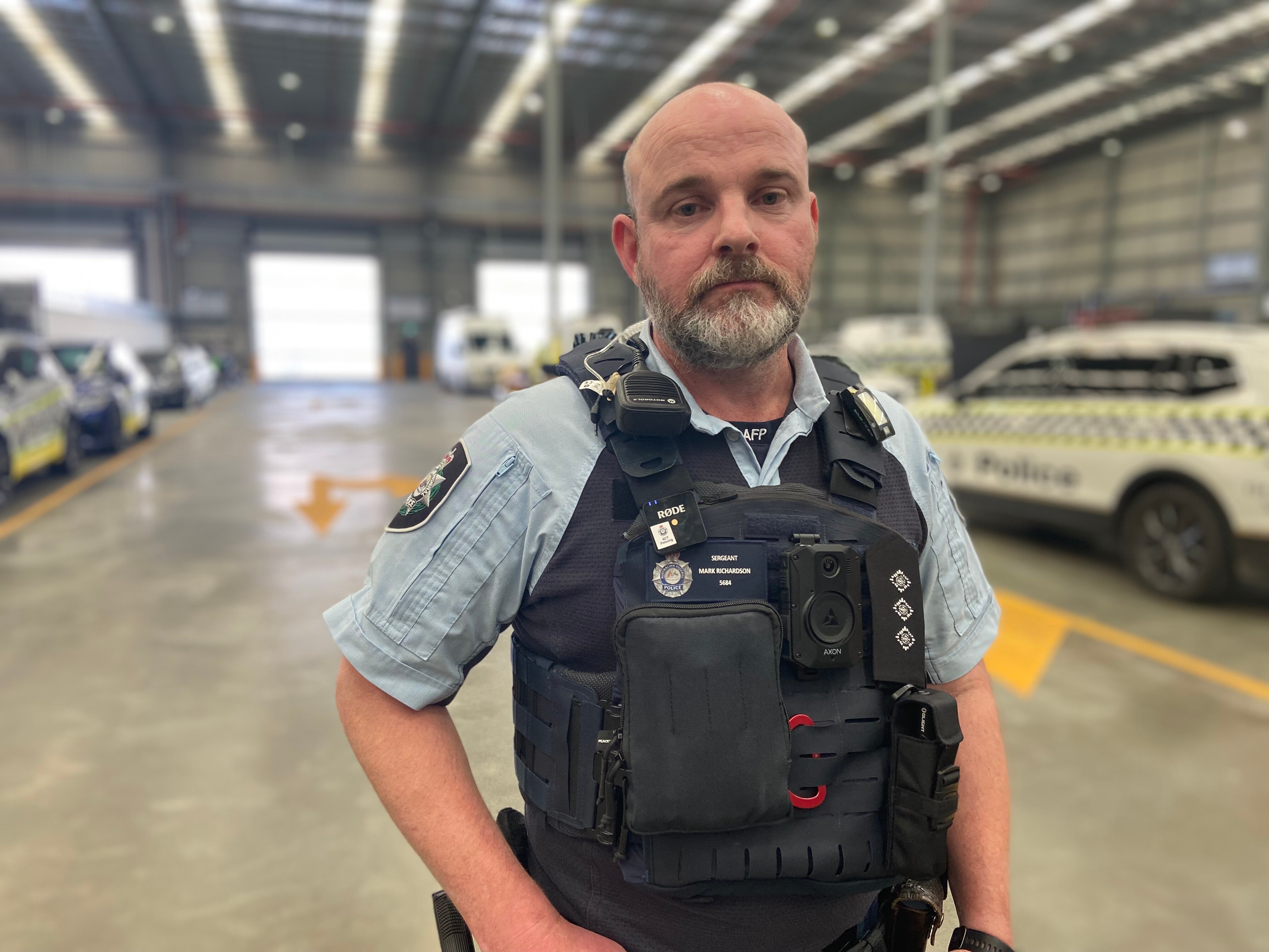 A man in a police uniform stands in a garage of police cars