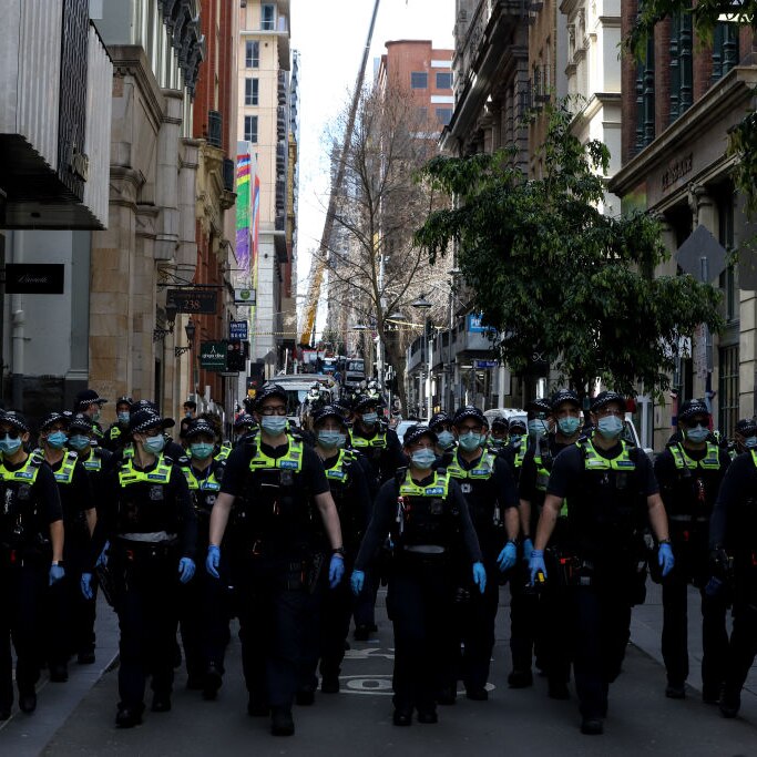 row of australian police in uniform wearing face masks and blue gloves on city street
