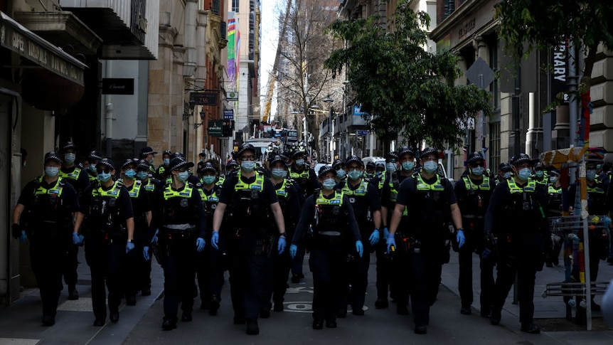 row of australian police in uniform wearing face masks and blue gloves on city street