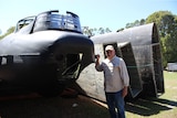 A man stands in a paddock next to a plane that is in pieces.
