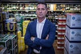 A politician in a suit standing in a liquor store after making an announcement about a Banned Drinkers Register.
