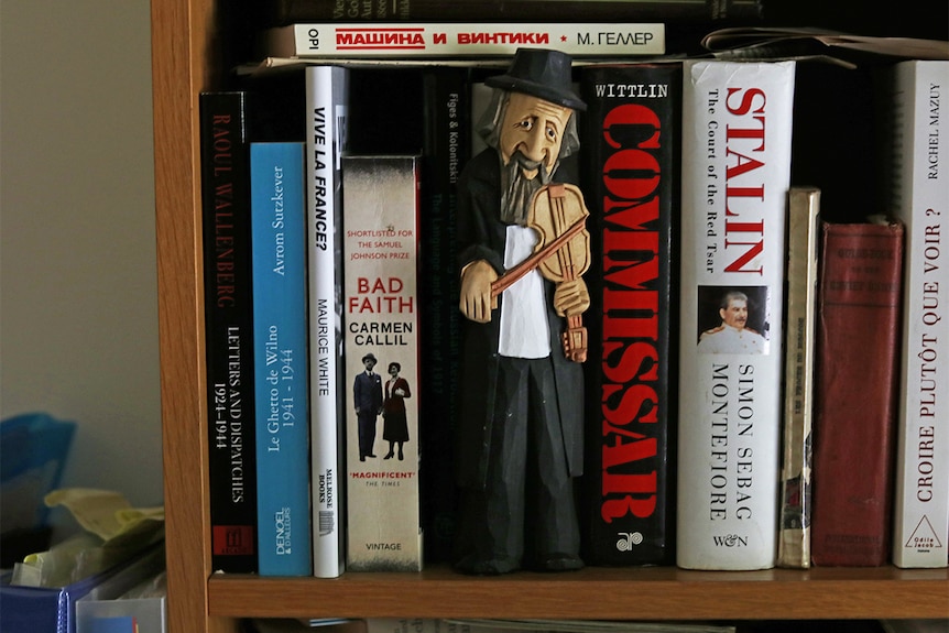 A bookshelf with books on communism and Stalin and a figurine of a bearded, hatted man playing fiddle.