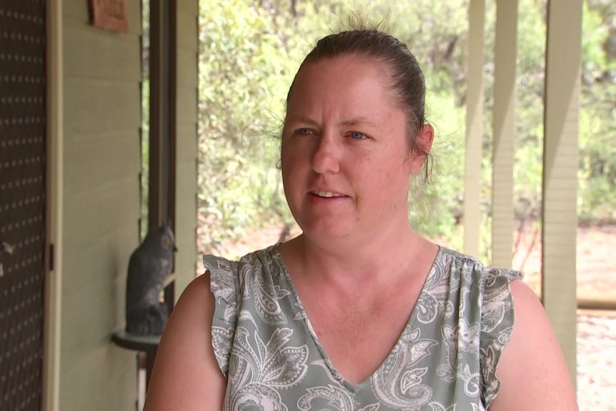 Leah Beard stands outside a house on a verandah with trees behind her