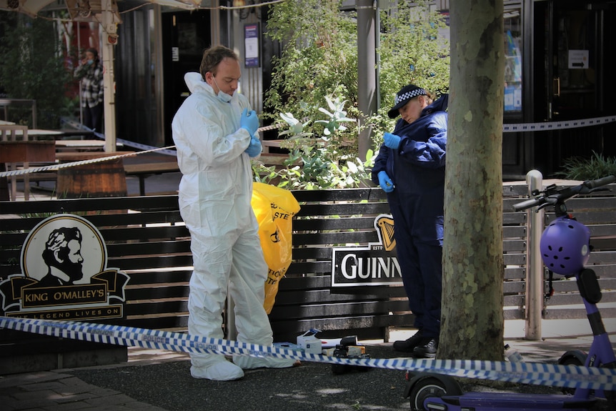 A man wearing a white hazmat suit stands near an area sectioned off by blue and white police tape