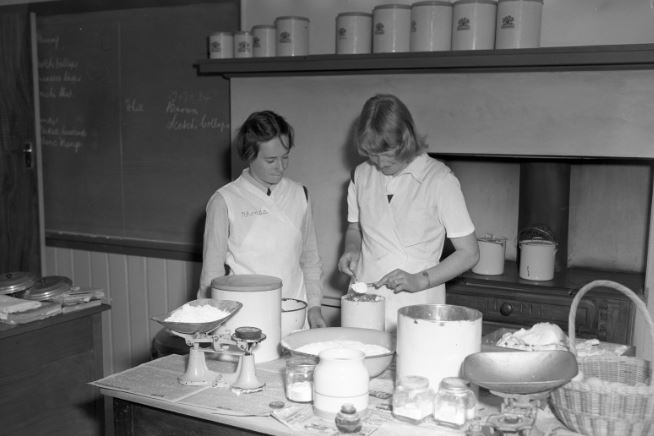 Black and White photo of two students taking a cooking class in high school.