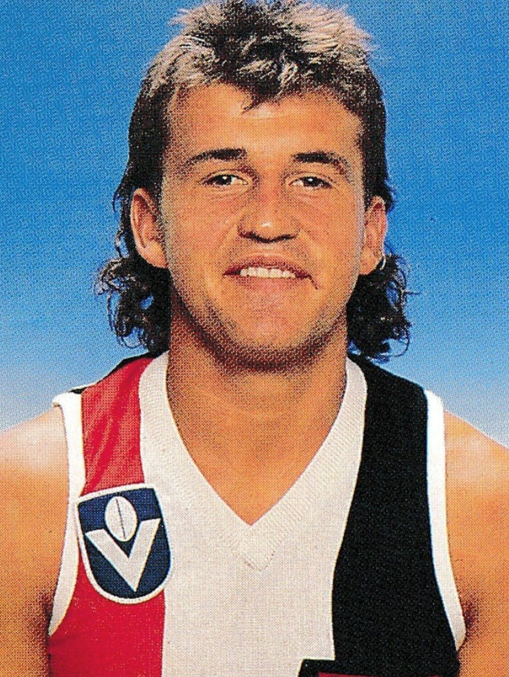 A man in a St Kilda jersey looks at the camera and smiles.