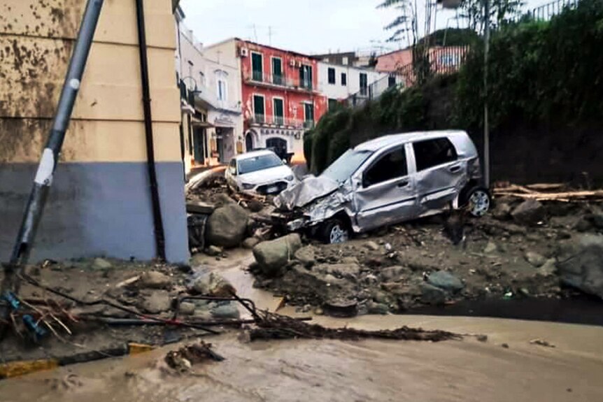 Destroyed cars scene on mud-lined street after landslide.