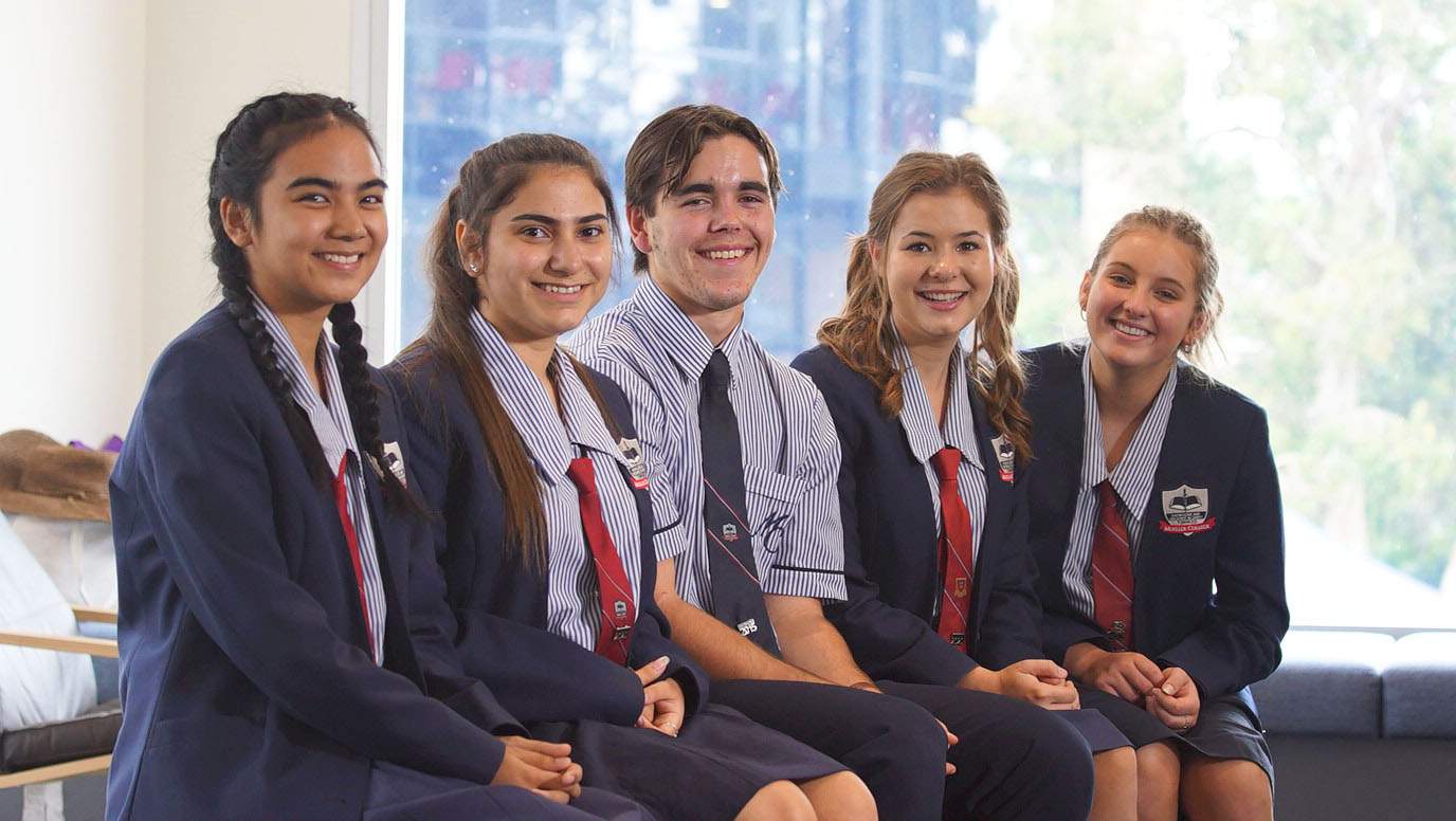 Five Year 12 students - four girls and a boy, from Mueller College, sit smiling as a group at Rothwell on Brisbane's northside.