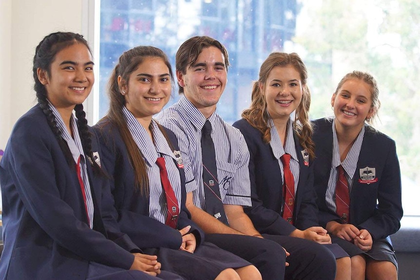 Five Year 12 students - four girls and a boy, from Mueller College, sit smiling as a group at Rothwell on Brisbane's northside.