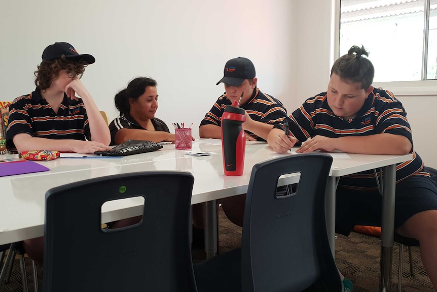 Callum (right) sit at a table with classmates and an assistant teacher