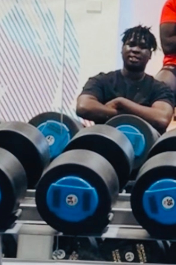 a young african man sitting behind weights at a gym
