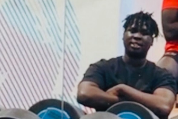 a young african man sitting behind weights at a gym