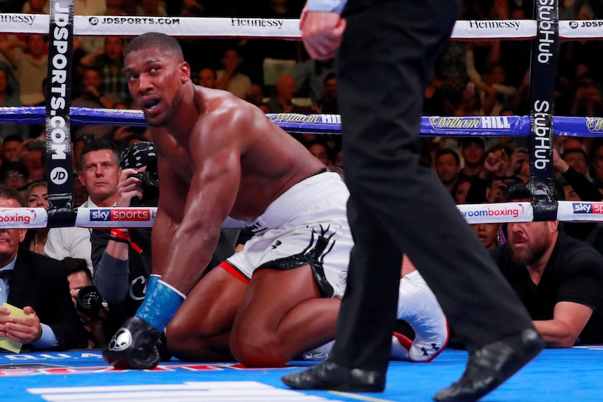 Anthony Joshua look up from his hands and knees at a man wearing dress trousers.
