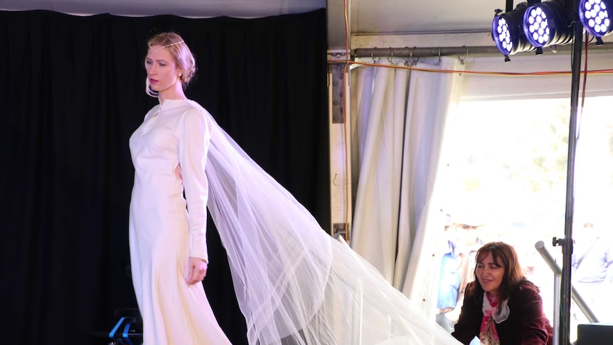 Eco Fashion Week Australia founder Zuhal Kuvan-Mills helping a model with wedding dress train.