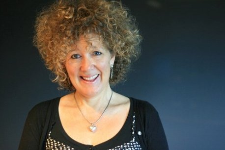 A middle-aged woman with voluminous blonde, curly hair, smiling.