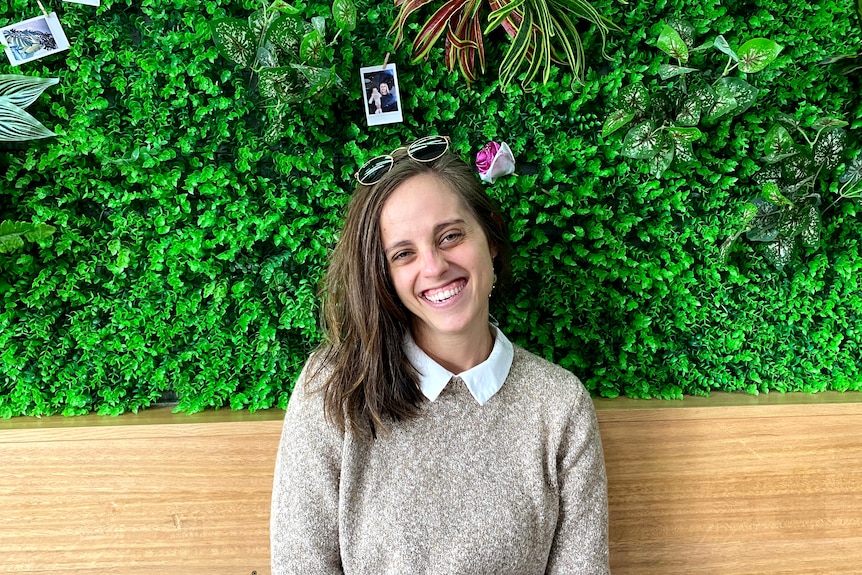 A young person with long hair sitting in front of a wall of green