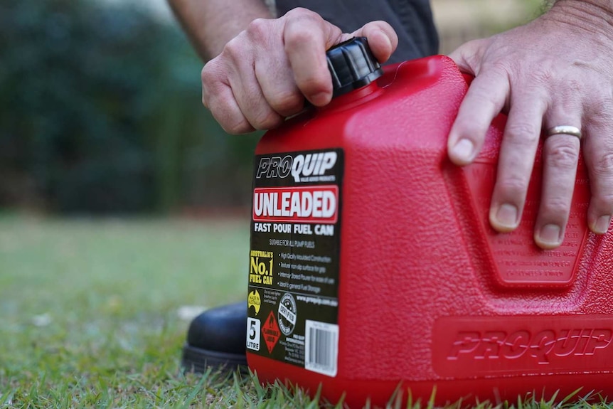 Man with wedding ring holds a red jerry can with petrol in it.