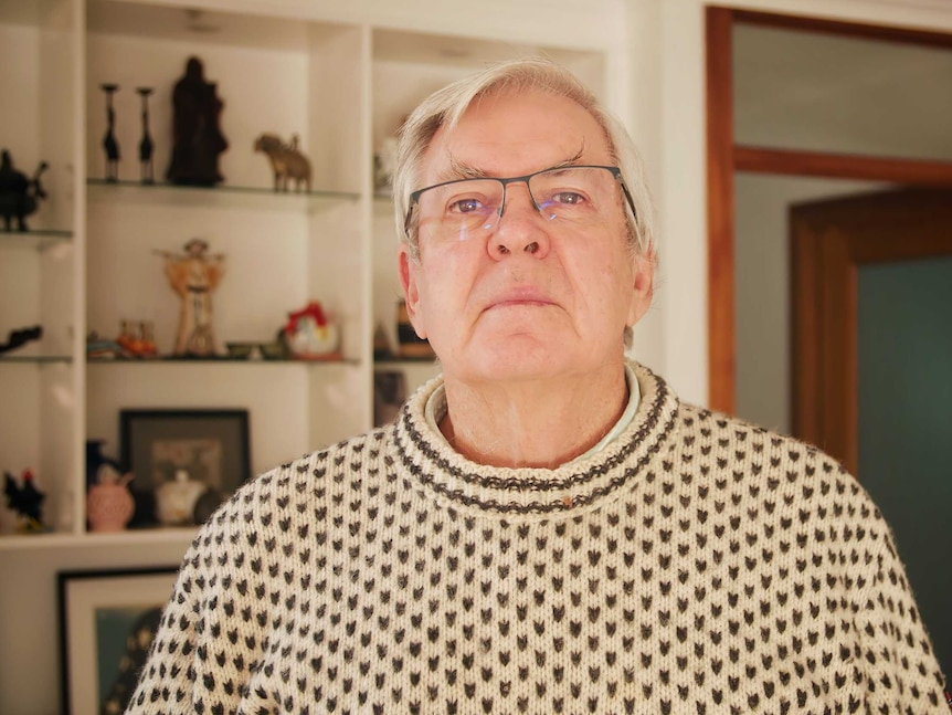 Professor Bob Gregory at his home in front of a shelf with trinkets.