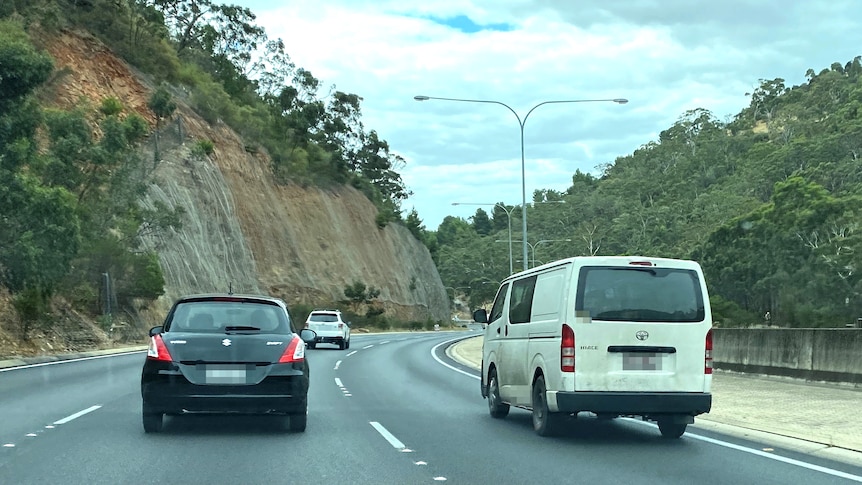 Vehicles drive on a multi-lane highway surrounded by hills
