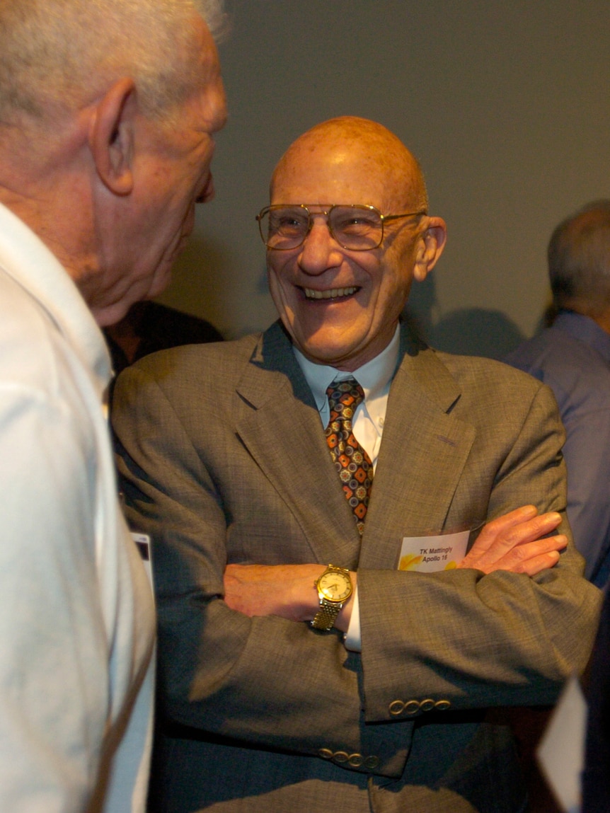 Man wearing a suit with arms crossed laughing as he faces another person