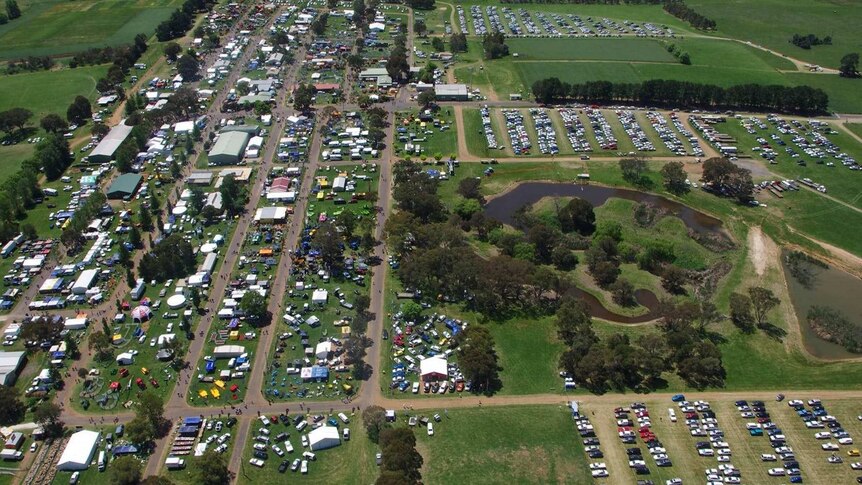 An aerial view of a field days with cars and people below and green graas