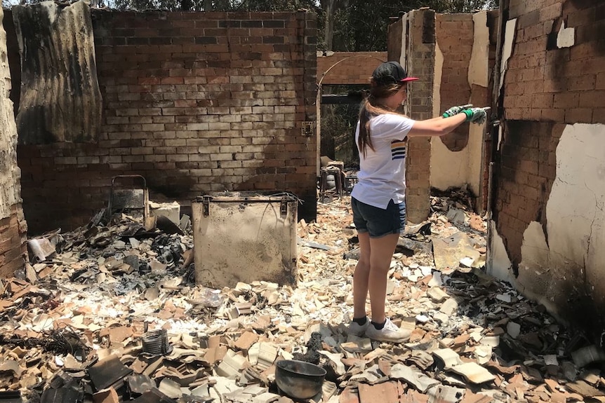 Estelle Webb standing on rubble and damaged bricks pointing at a brick wall