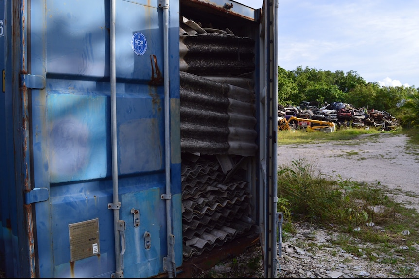 A blue shipping container's door is open, and sheets of asbestos are packed to the top.