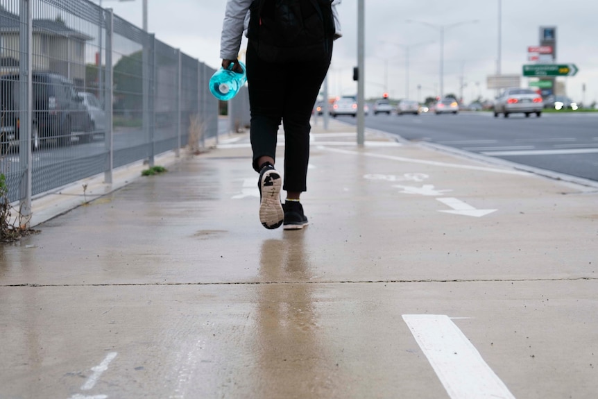 Backpack and legs of a teenage girl walking on a footpath beside a busy outer Melbourne road