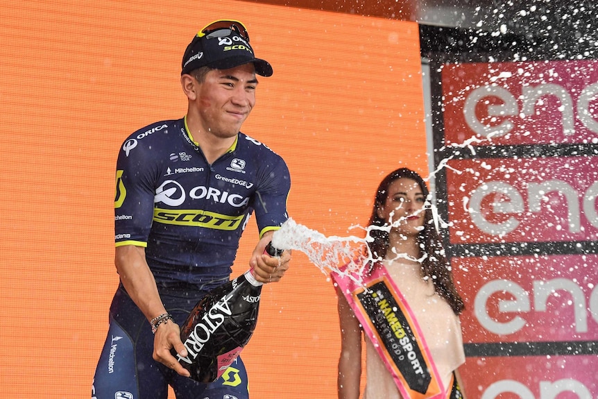 Caleb Ewan sprays champagne wearing a dark blue jersey