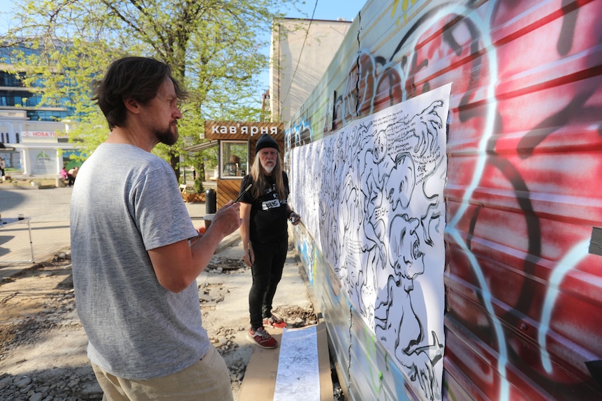 George Gittoes paints a street mural in Ukraine with another man.