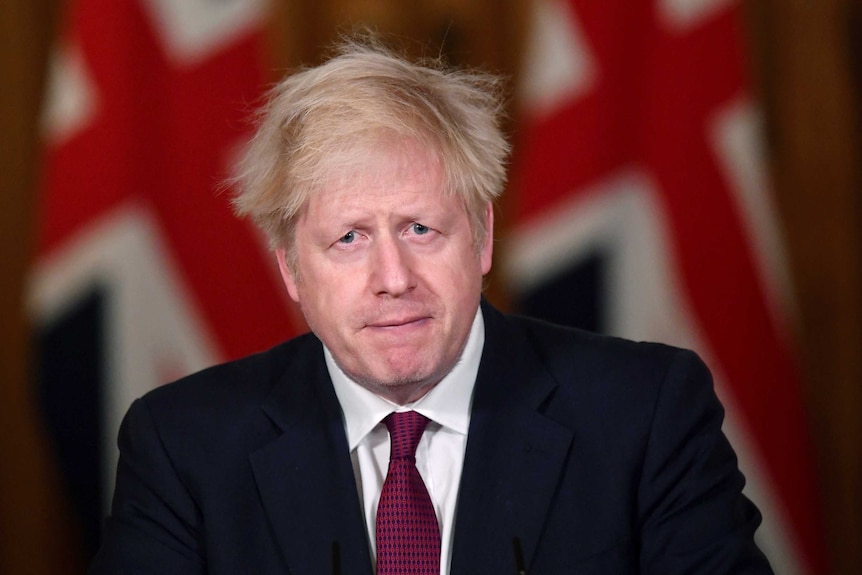 Boris Johnson with pursed lips and worried eyes speaks at a podium.