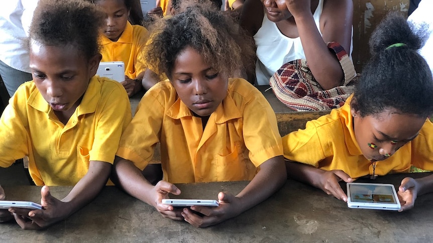 School children in yellow uniforms read from the Library for All app.