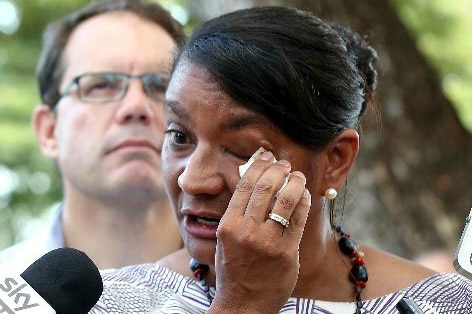 Nova Peris wipes a tear from her eye as she stands in front of microphones.