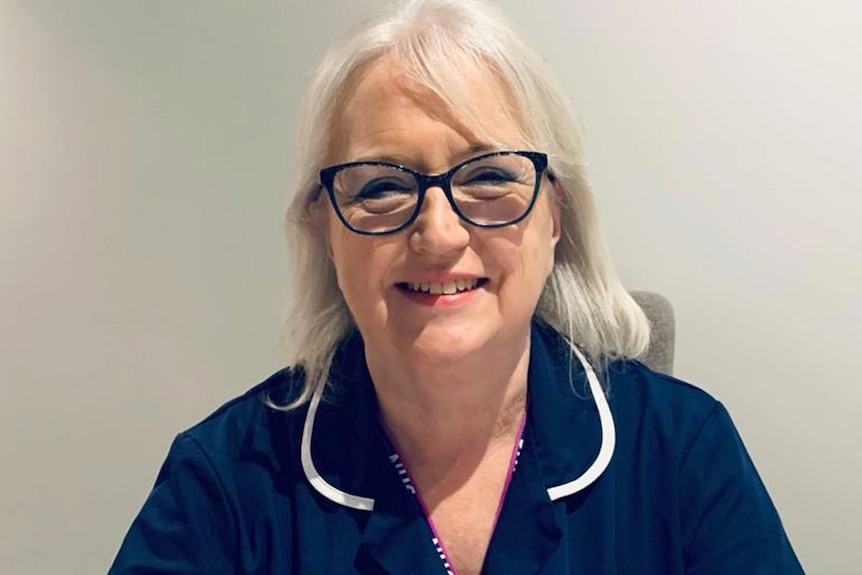 A woman in black spectacles and a nurse's uniform poses for a photo