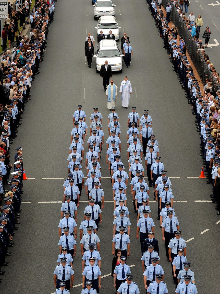 Thousands of mourners line the Gold Coast Highway as Senior Constable Damian Leeding's body is led away in a funeral procession.